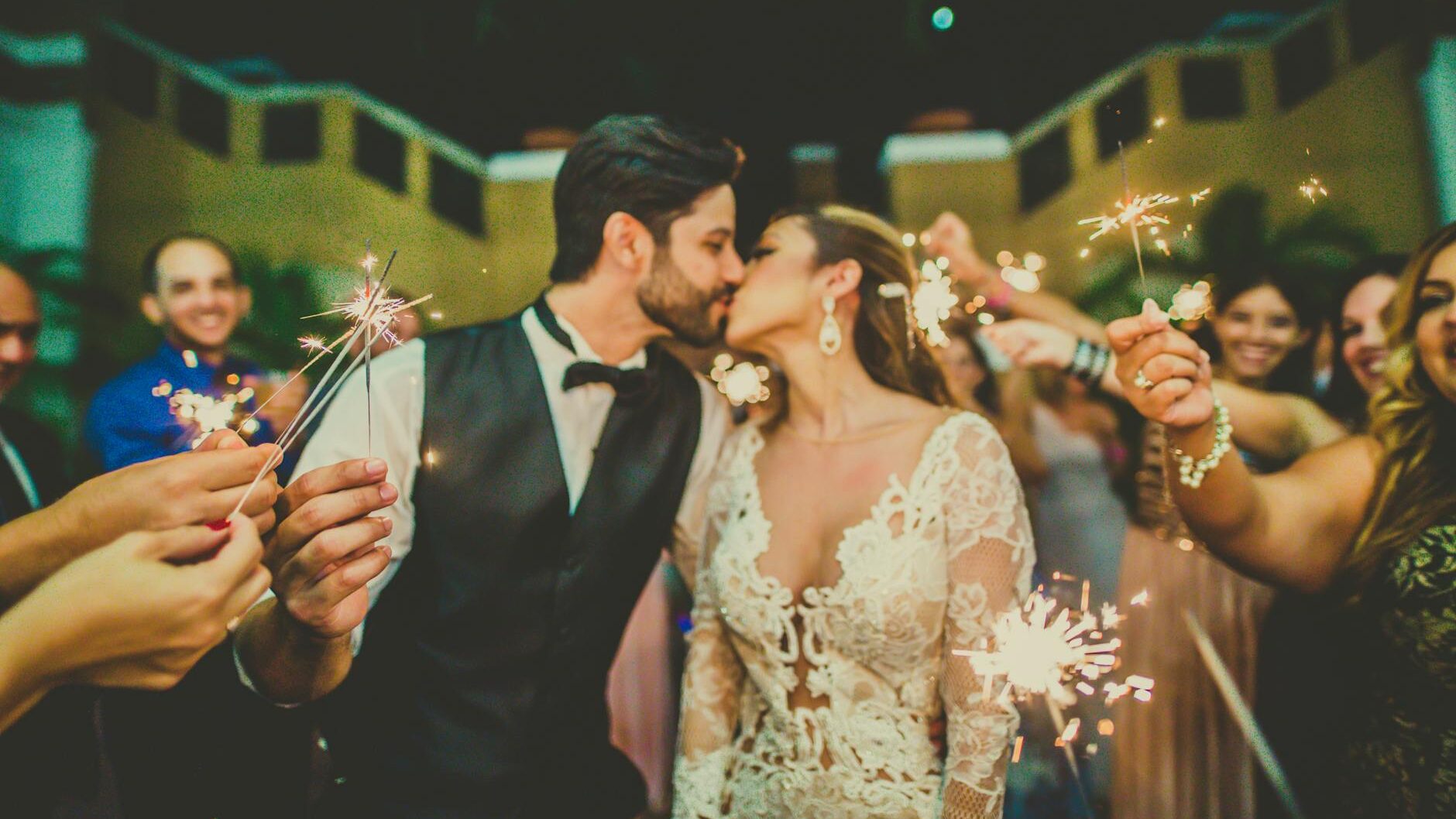 photo of couple kissing near people holding sparklers