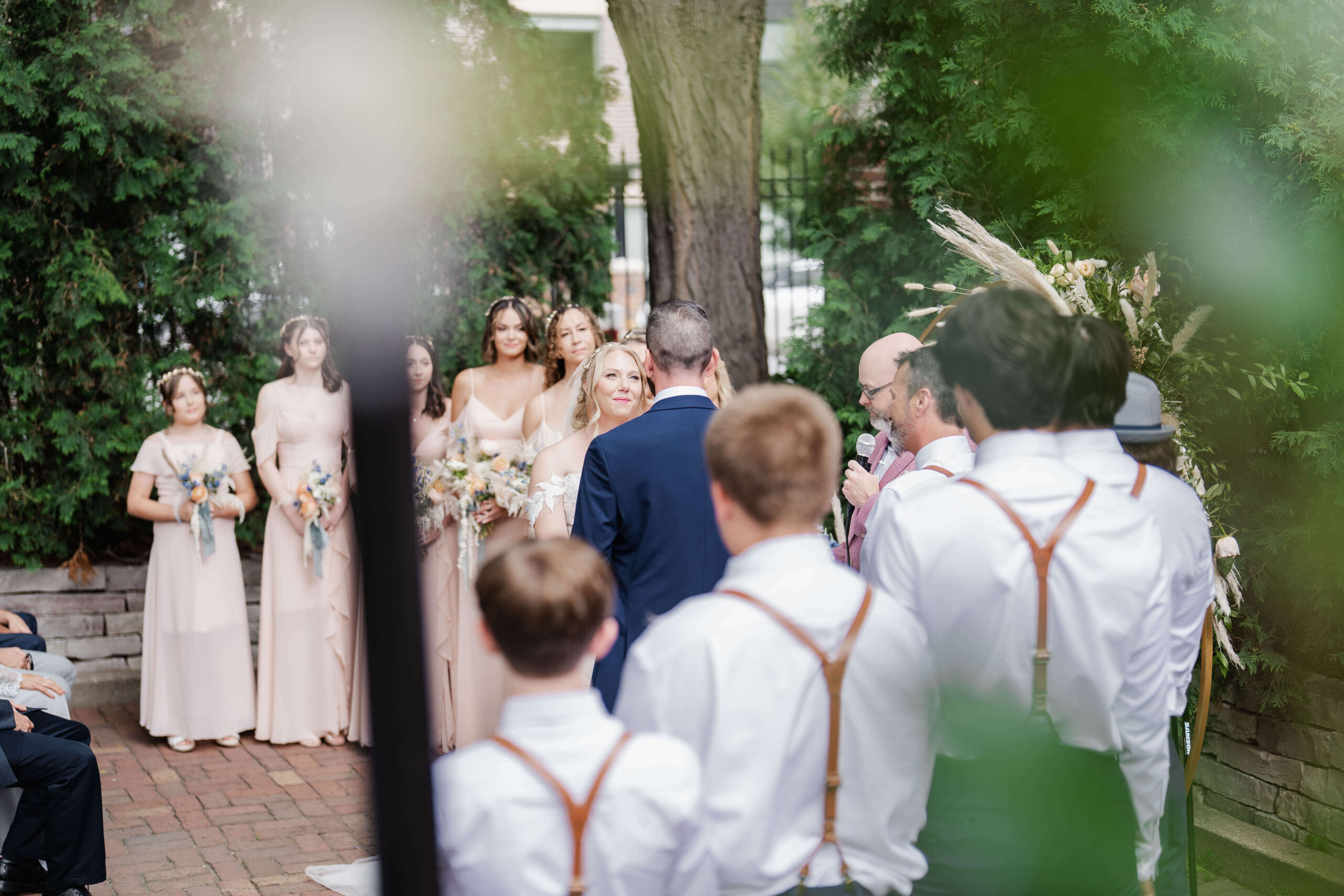 Bride and groom exchange vows in an outdoor ceremony with bridesmaids and groomsmen in attendance.